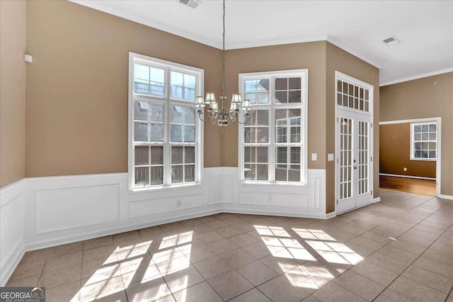 unfurnished dining area featuring a wainscoted wall, tile patterned flooring, crown molding, french doors, and a notable chandelier