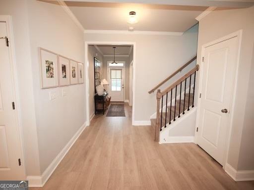 hall featuring light wood finished floors, crown molding, stairs, and baseboards