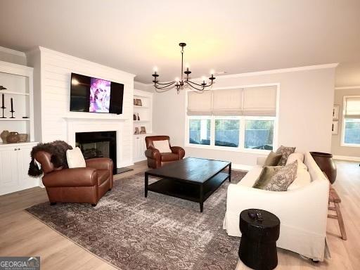 living area with a chandelier, a fireplace with raised hearth, wood finished floors, and crown molding