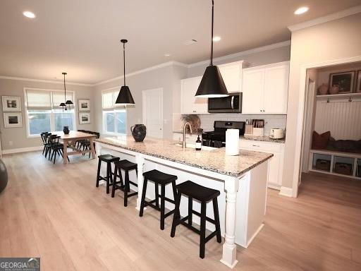 kitchen featuring stainless steel microwave, crown molding, a kitchen bar, black range oven, and white cabinets