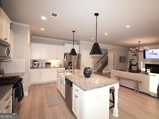 kitchen with light wood-type flooring, tasteful backsplash, white cabinetry, appliances with stainless steel finishes, and crown molding