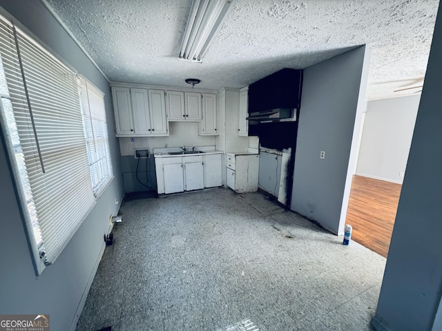 kitchen with a textured ceiling, under cabinet range hood, a sink, baseboards, and light countertops