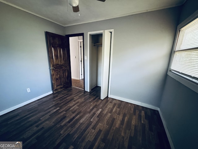 unfurnished bedroom featuring crown molding, dark wood finished floors, a closet, ceiling fan, and baseboards