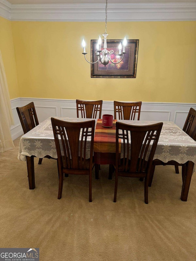 dining area with ornamental molding, a wainscoted wall, light colored carpet, and a notable chandelier