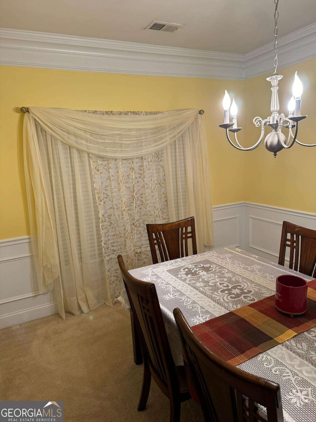 carpeted dining room with a chandelier, ornamental molding, a wainscoted wall, and visible vents