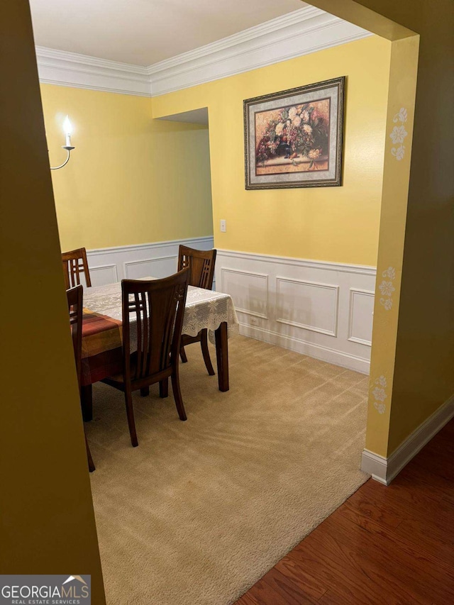 carpeted dining area featuring a wainscoted wall, wood finished floors, and crown molding