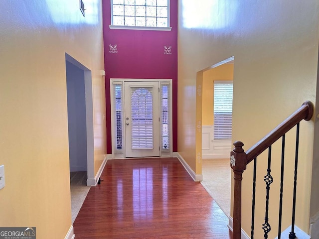 foyer entrance with a healthy amount of sunlight, a towering ceiling, and wood finished floors