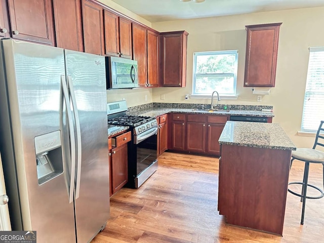 kitchen with a breakfast bar area, appliances with stainless steel finishes, a sink, dark stone countertops, and light wood-type flooring