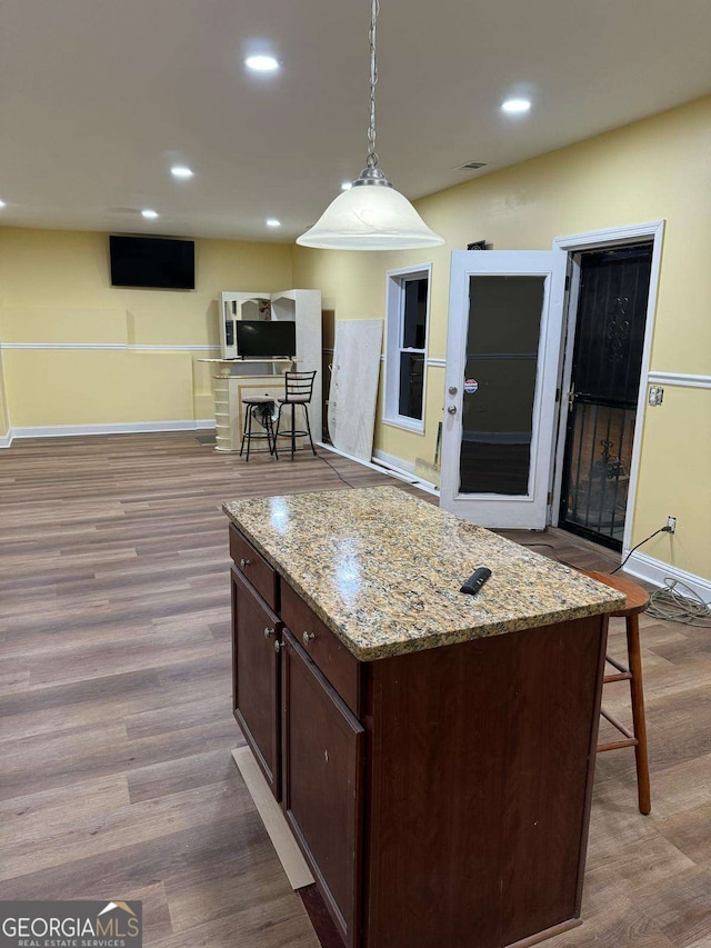 kitchen featuring dark brown cabinetry, recessed lighting, wood finished floors, hanging light fixtures, and light stone countertops