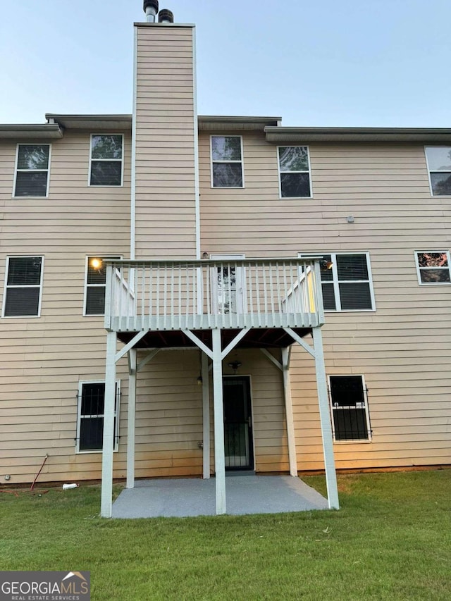 rear view of property with a deck, a yard, a chimney, and a patio area