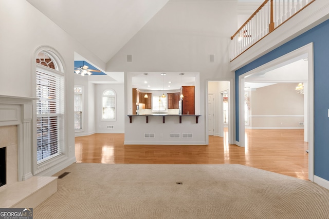 unfurnished living room with a chandelier, light colored carpet, a premium fireplace, visible vents, and light wood finished floors