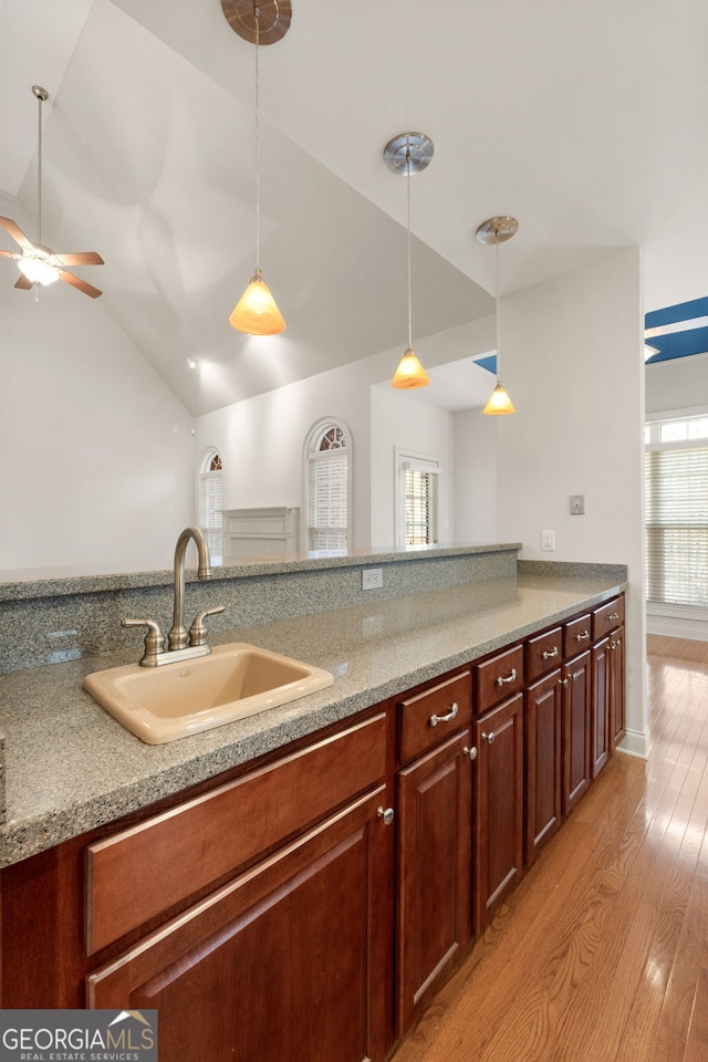 kitchen featuring lofted ceiling, light countertops, hanging light fixtures, a sink, and light wood-type flooring