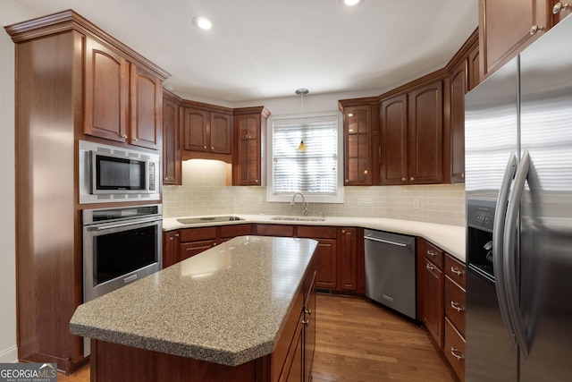 kitchen with pendant lighting, stainless steel appliances, backsplash, a sink, and wood finished floors