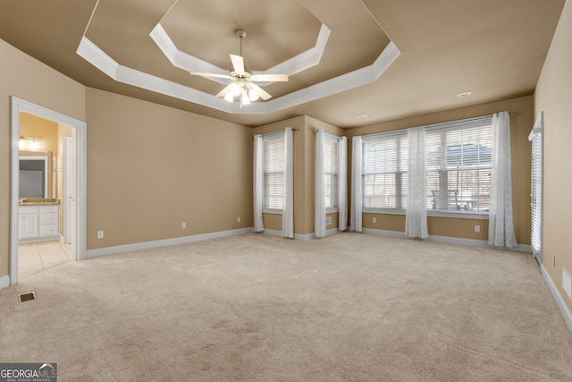 unfurnished room with a tray ceiling, carpet flooring, crown molding, and visible vents