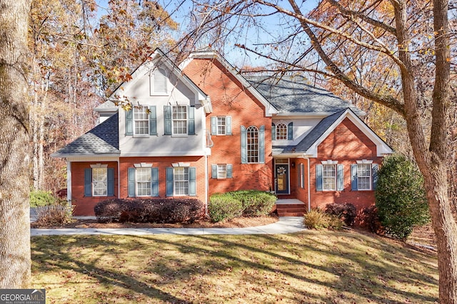 traditional-style home featuring roof with shingles, brick siding, and a front lawn