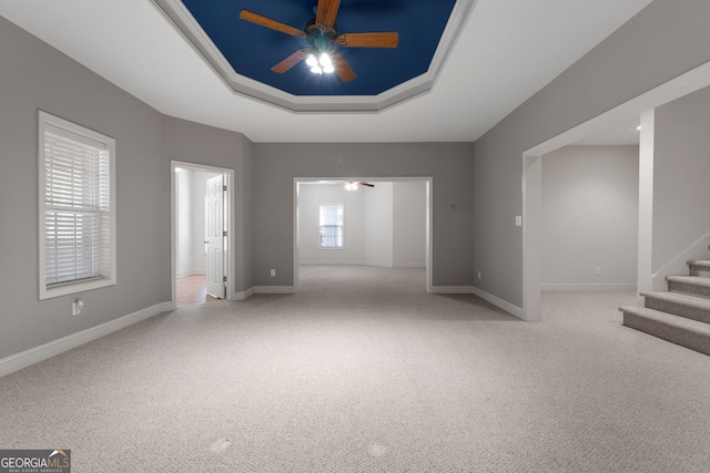 unfurnished room with a raised ceiling, a ceiling fan, carpet flooring, baseboards, and stairs