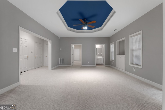 unfurnished bedroom featuring baseboards, visible vents, a raised ceiling, light colored carpet, and ensuite bath