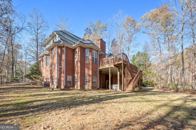 rear view of house with brick siding, a chimney, a lawn, a deck, and stairs