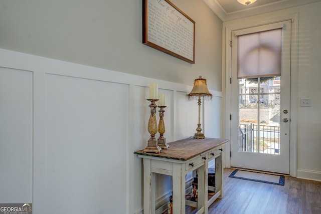 doorway featuring a wainscoted wall, ornamental molding, wood finished floors, and a decorative wall