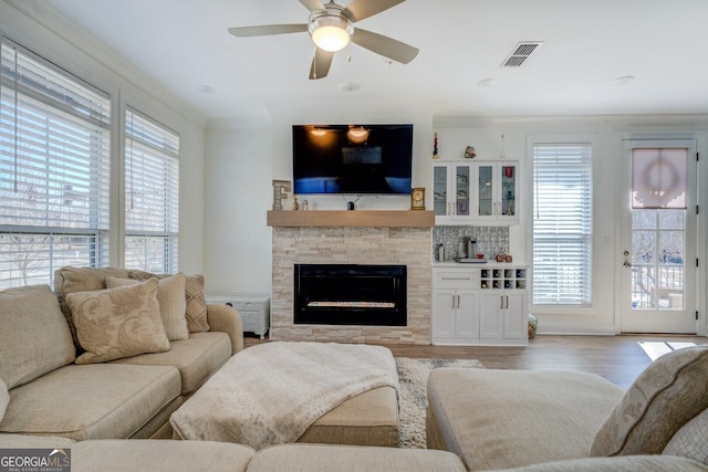 living area with visible vents, a stone fireplace, a wealth of natural light, and light wood-style floors