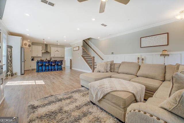 living room with ornamental molding, stairway, light wood-style flooring, and visible vents