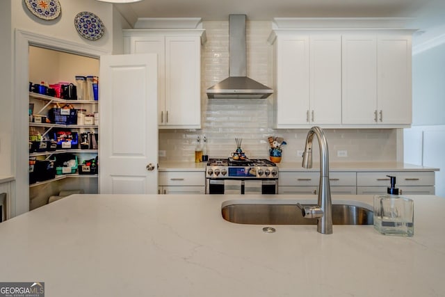 kitchen with a sink, wall chimney exhaust hood, white cabinetry, and stainless steel range with gas stovetop