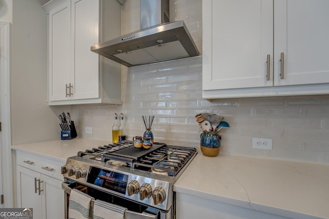 kitchen with stainless steel gas stove, wall chimney range hood, white cabinets, and backsplash