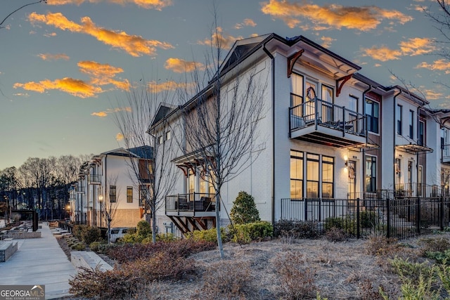 property exterior at dusk featuring brick siding, fence, and a balcony