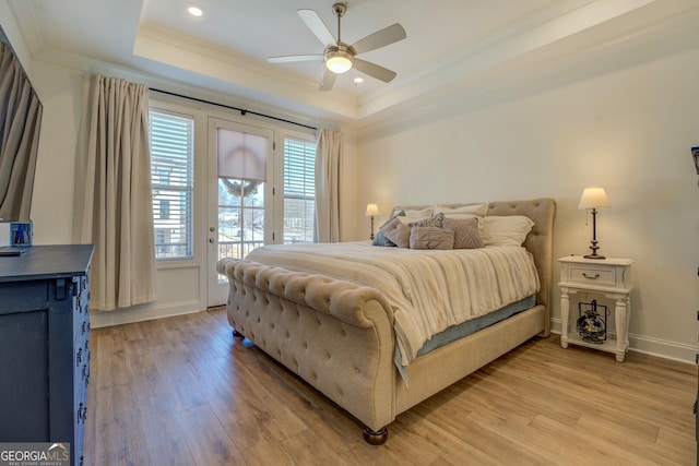 bedroom with crown molding, a tray ceiling, light wood-type flooring, and access to exterior