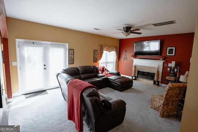 carpeted living room with a glass covered fireplace, visible vents, and ceiling fan