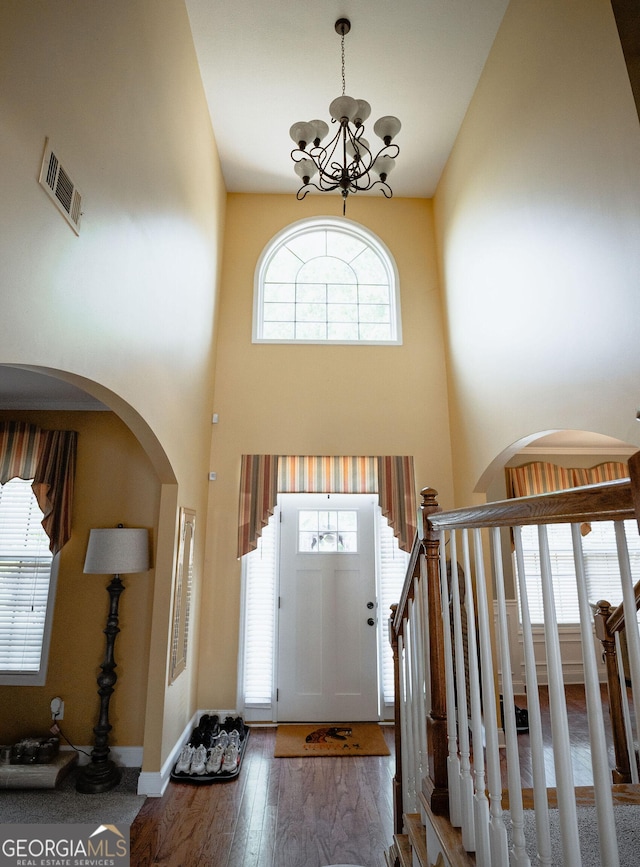 entryway featuring arched walkways, visible vents, stairway, wood finished floors, and a chandelier