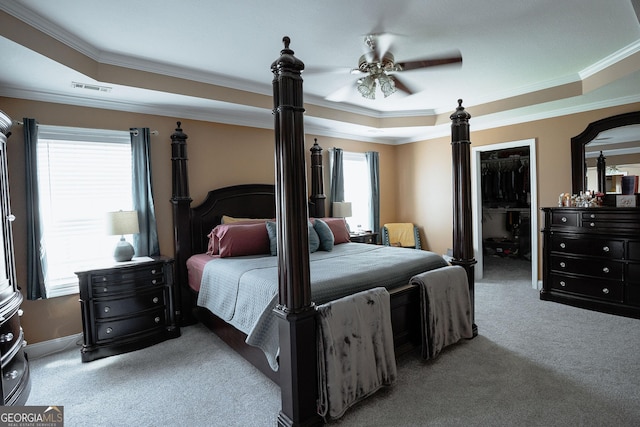 bedroom with visible vents, carpet, a tray ceiling, a walk in closet, and crown molding