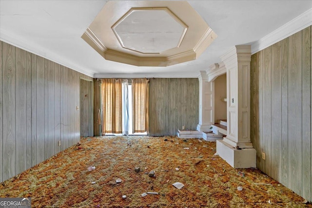 empty room featuring ornamental molding, a tray ceiling, wood walls, and decorative columns