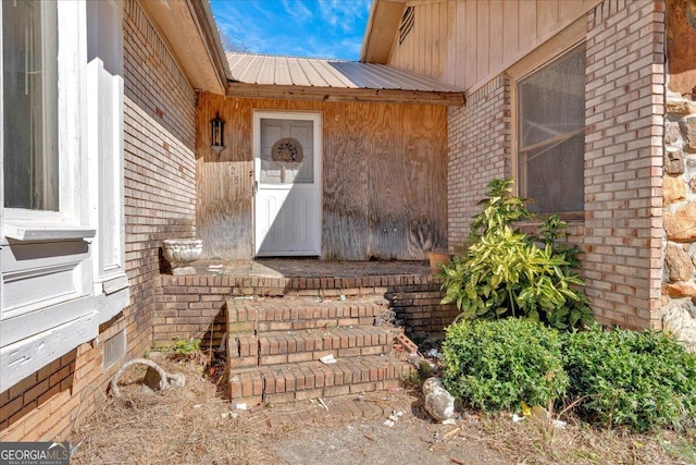 entrance to property featuring brick siding and metal roof