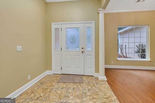 foyer entrance featuring crown molding, wood finished floors, baseboards, and ornate columns