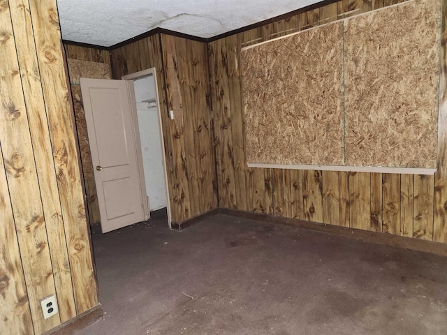 unfurnished room with wood walls, a textured ceiling, crown molding, and baseboards