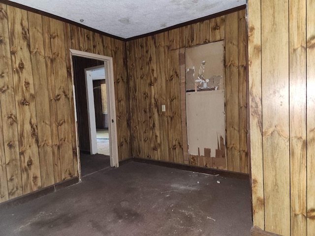 spare room featuring wooden walls, a textured ceiling, baseboards, and ornamental molding