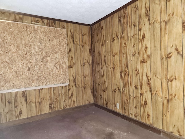 empty room featuring crown molding, wooden walls, and concrete floors