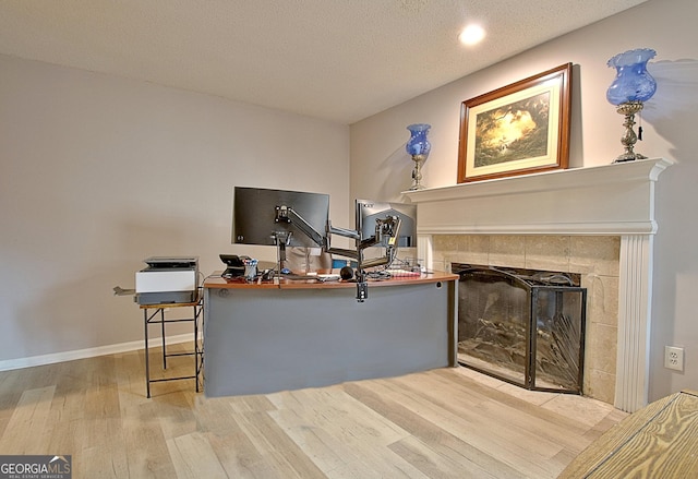 office space with a fireplace, a textured ceiling, baseboards, and wood finished floors