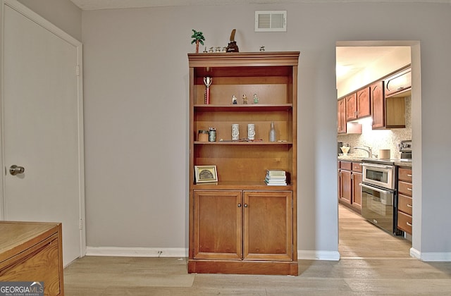 bar with range with two ovens, a sink, visible vents, light wood finished floors, and tasteful backsplash