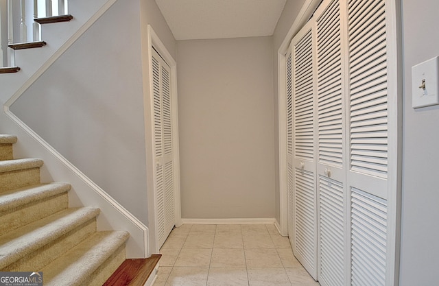 corridor with light tile patterned floors, baseboards, and stairs