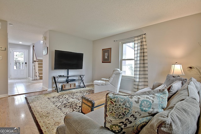 living room featuring hardwood / wood-style flooring, a textured ceiling, baseboards, and stairs