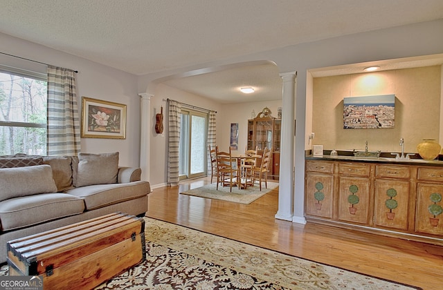 living room featuring a textured ceiling, light wood-type flooring, baseboards, and ornate columns