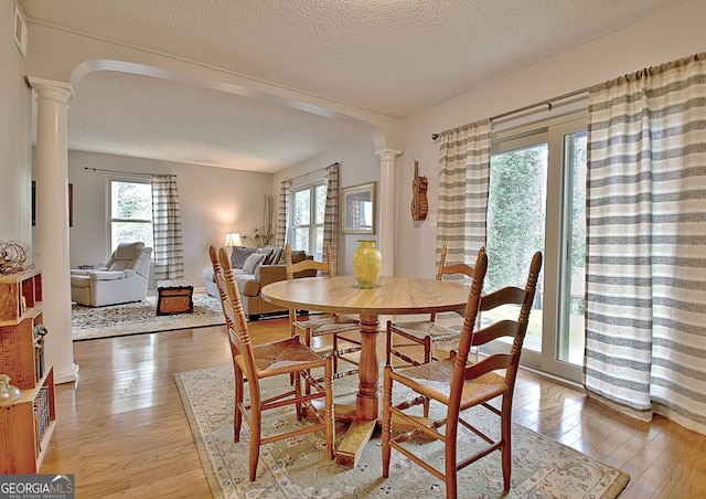 dining space featuring plenty of natural light, light wood finished floors, decorative columns, and arched walkways