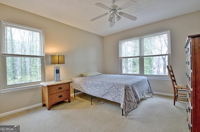 bedroom with a ceiling fan, light colored carpet, a textured ceiling, and baseboards