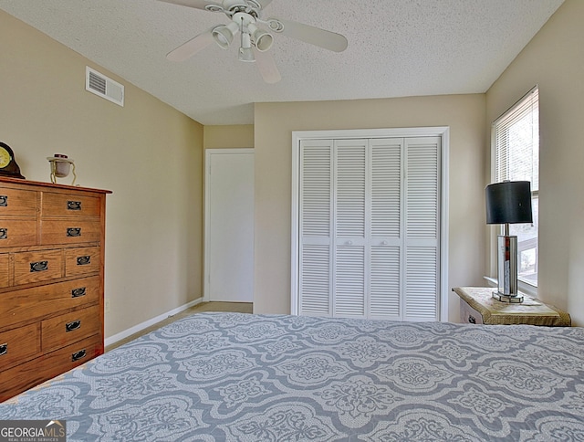 bedroom with a textured ceiling, visible vents, baseboards, a ceiling fan, and a closet