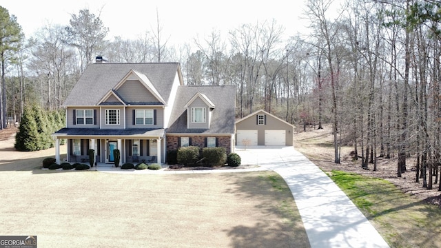 view of front of house with a shingled roof, a detached garage, a porch, an outbuilding, and driveway