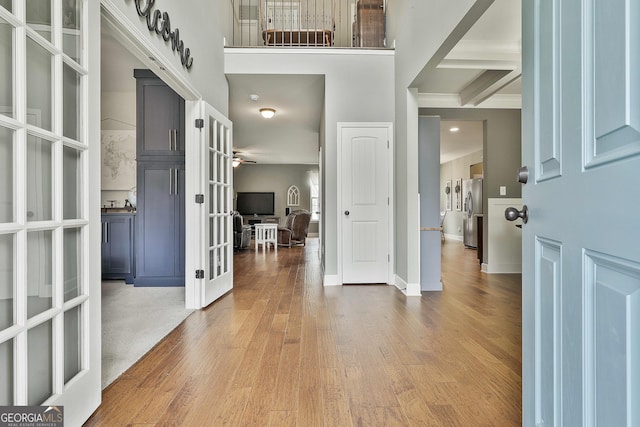 entryway featuring wood finished floors, baseboards, beam ceiling, french doors, and a towering ceiling