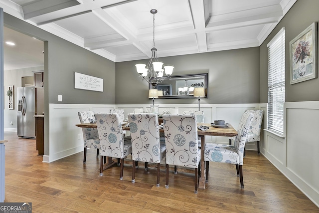 dining area featuring beamed ceiling, a wainscoted wall, coffered ceiling, wood finished floors, and a chandelier