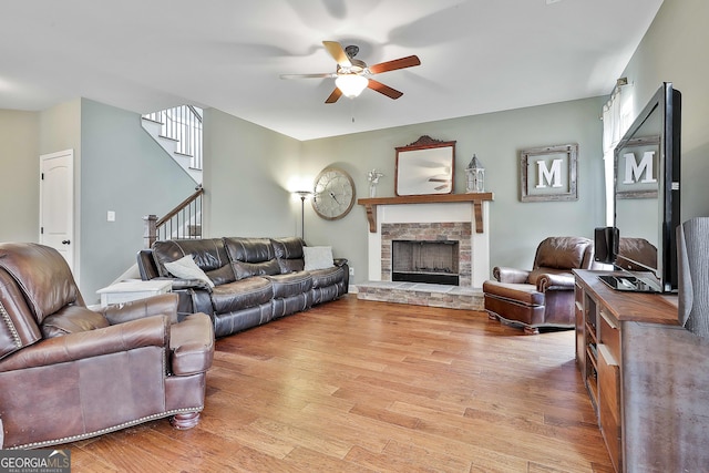 living room featuring a fireplace, stairway, a ceiling fan, and light wood finished floors